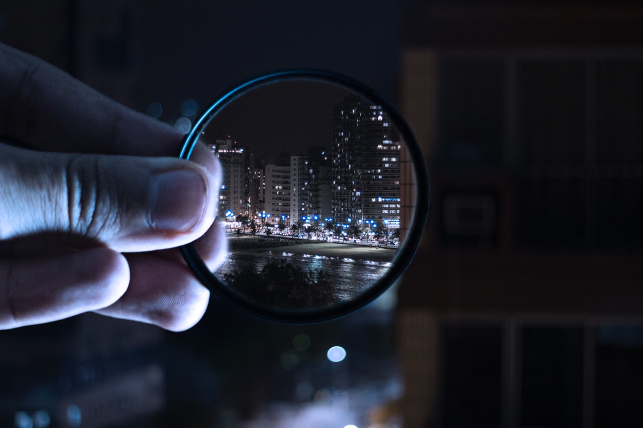 person holding magnifying glass looking at city